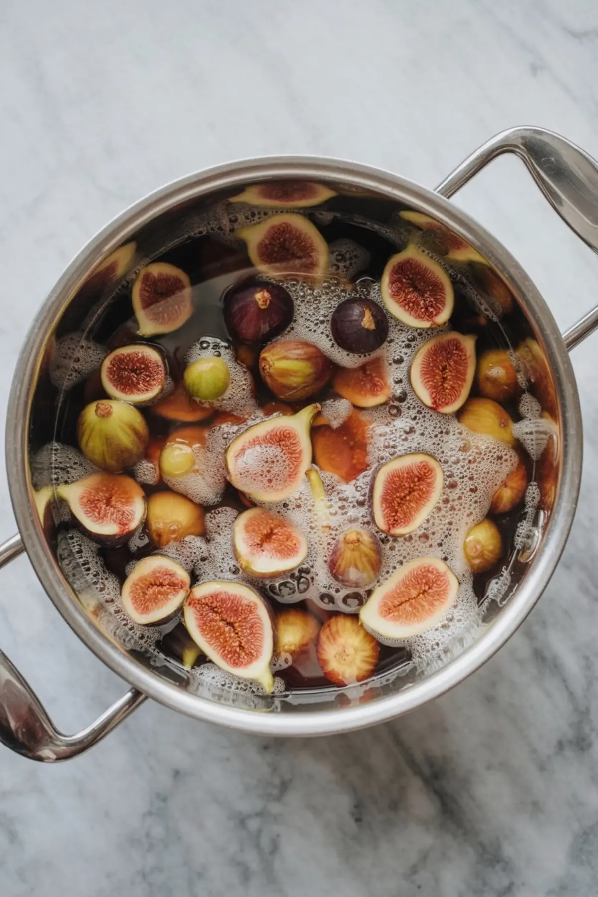 Overhead view of halved and whole figs simmering in a pot of bubbling liquid, beginning the process of making fig preserves.