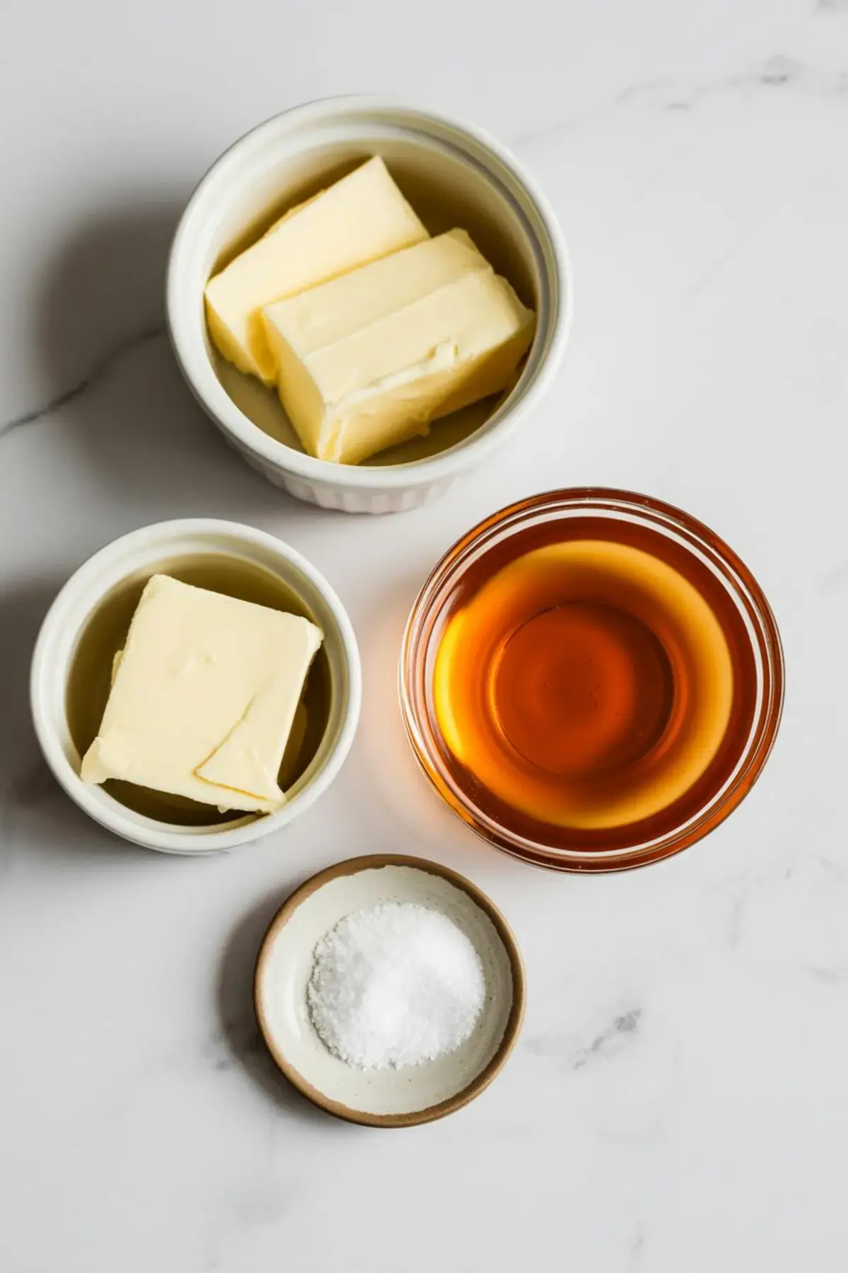 Small bowls filled with butter, maple syrup, and sea salt on a white surface, ready for making maple butter.