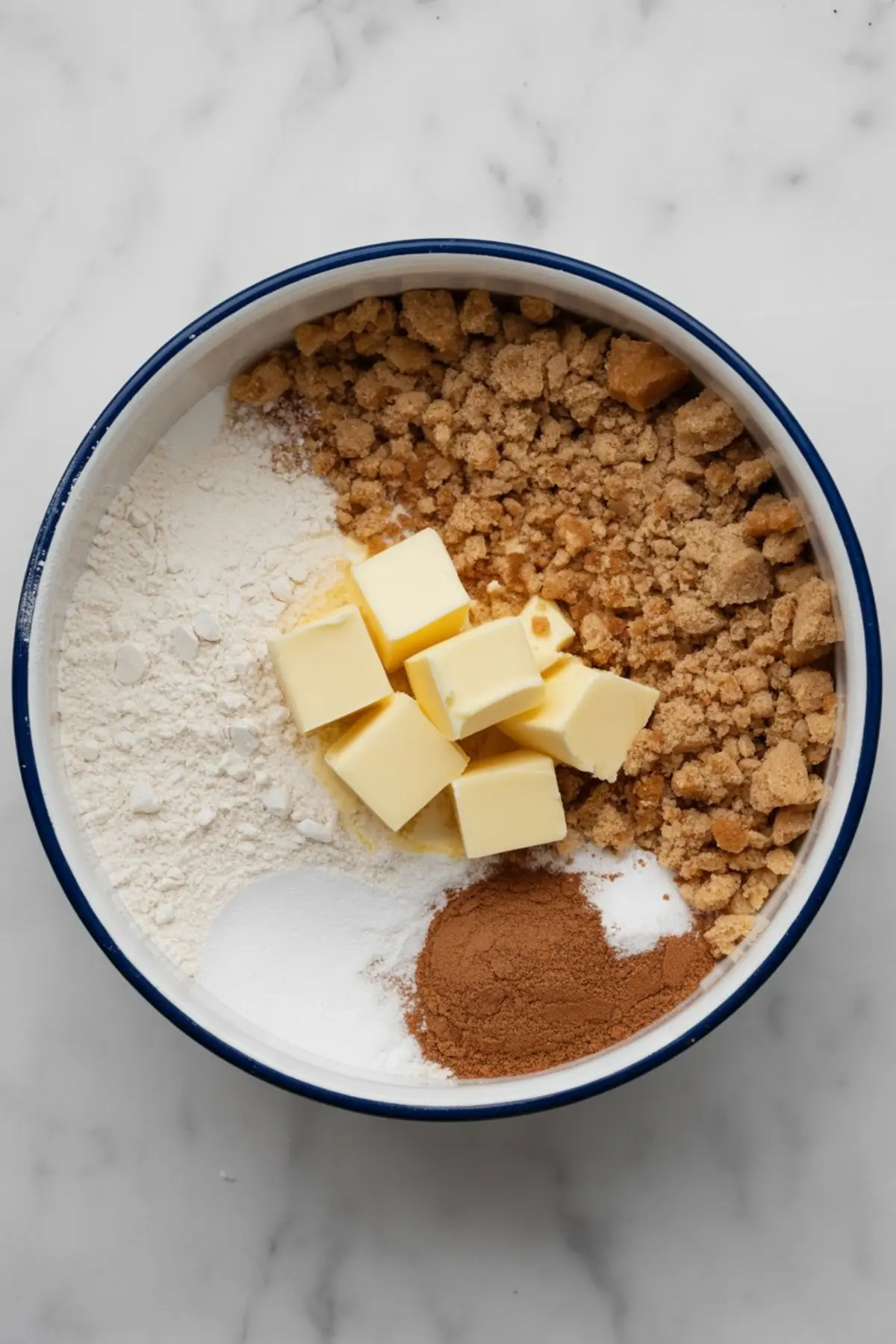 Mixing bowl filled with brown sugar, all-purpose flour, granulated sugar, cubed butter, and ground cinnamon, shown before blending to make a crumble topping.