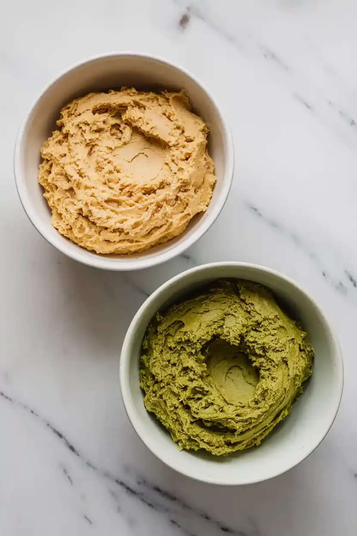 Two bowls of cookie dough side by side, one filled with green matcha dough and the other with pale vanilla dough, ready for baking.
