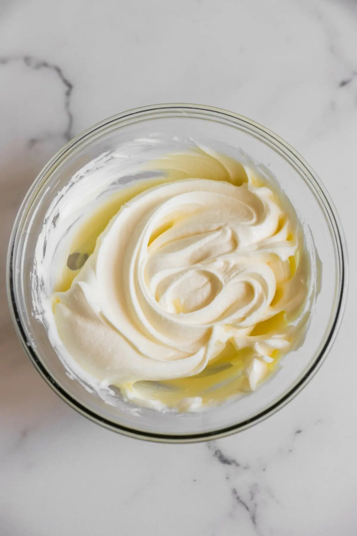 Bowl of smooth, whipped cream cheese mixture with visible swirls, prepared as a base for a creamy cheesecake filling.