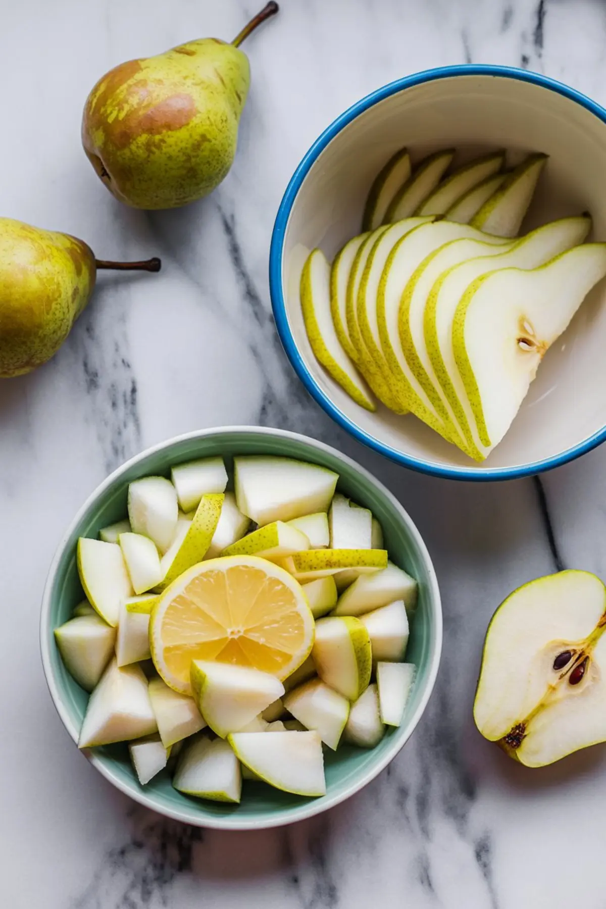 Fresh green pears sliced and chopped in two separate bowls with a lemon half in the center, placed on a white marble background.