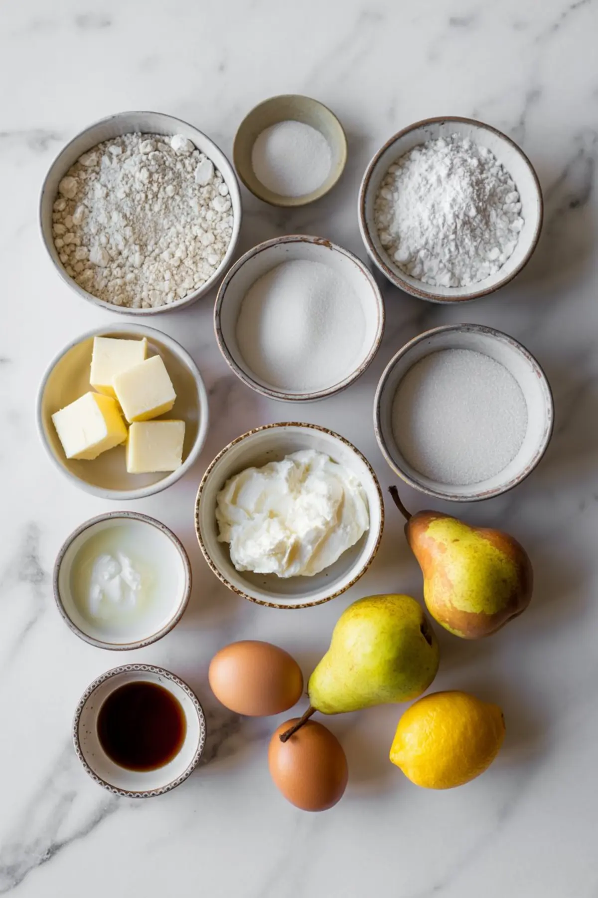 Overhead image of pear cake ingredients on a marble surface, including flour, butter, sugar, eggs, yogurt, ricotta, vanilla extract, baking powder, baking soda, fresh pears, and a lemon.