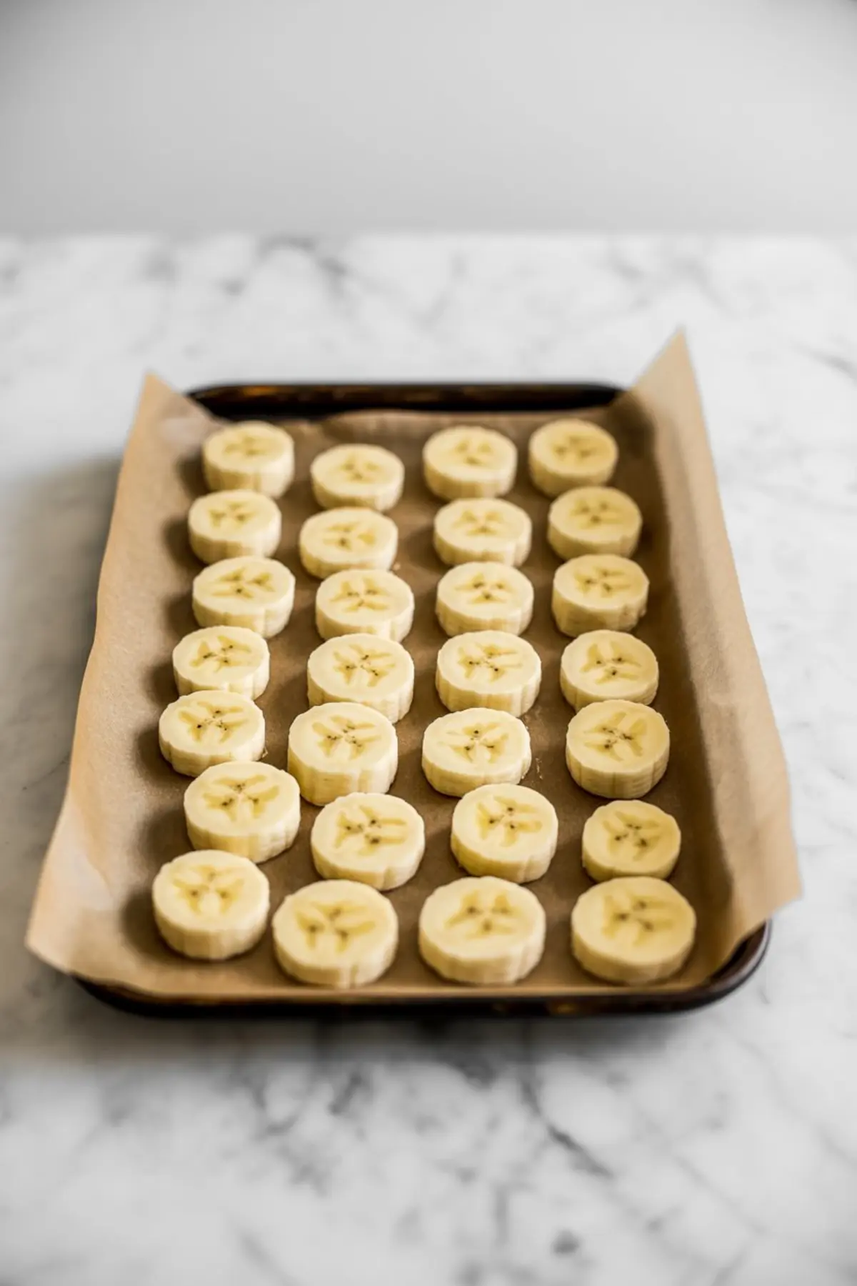 Neat rows of coin-cut banana pieces rest on a parchment-lined baking sheet, freezing for an easy no-churn banana ice cream base.