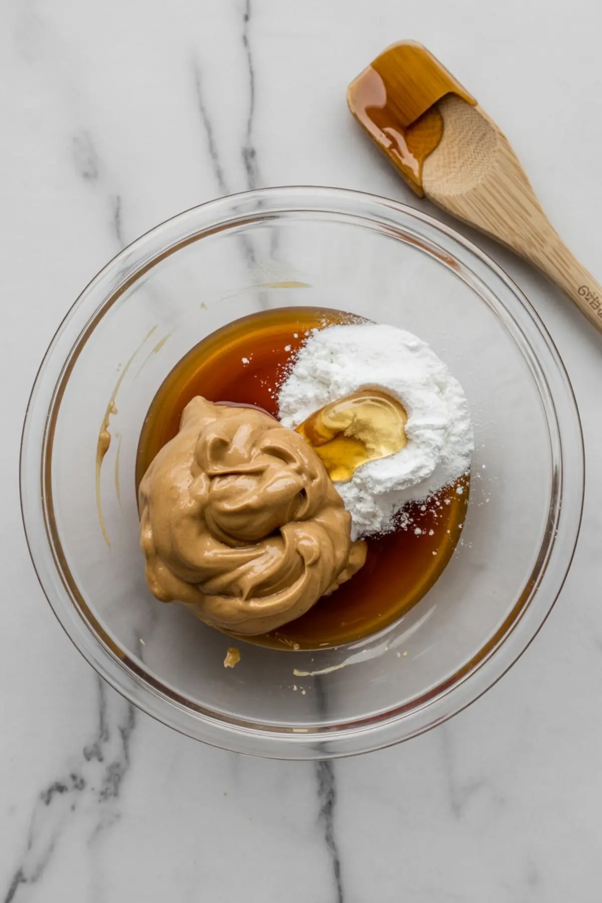 Mixing bowl containing peanut butter, maple syrup, protein powder, and honey, ready for blending into a sweet energy snack mix.