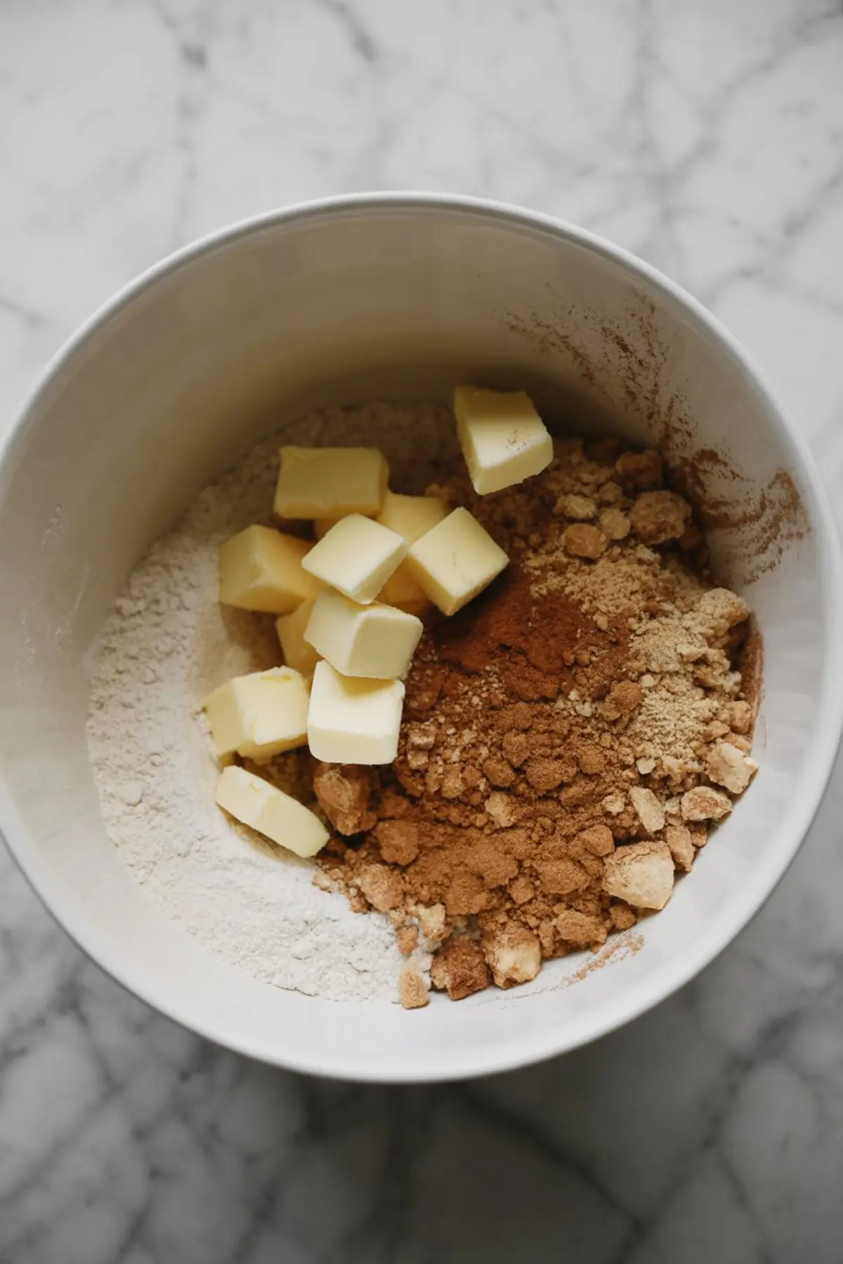 Dry crumb topping ingredients in a large mixing bowl, including cubed butter, flour, brown sugar, cinnamon, and ground ginger.
