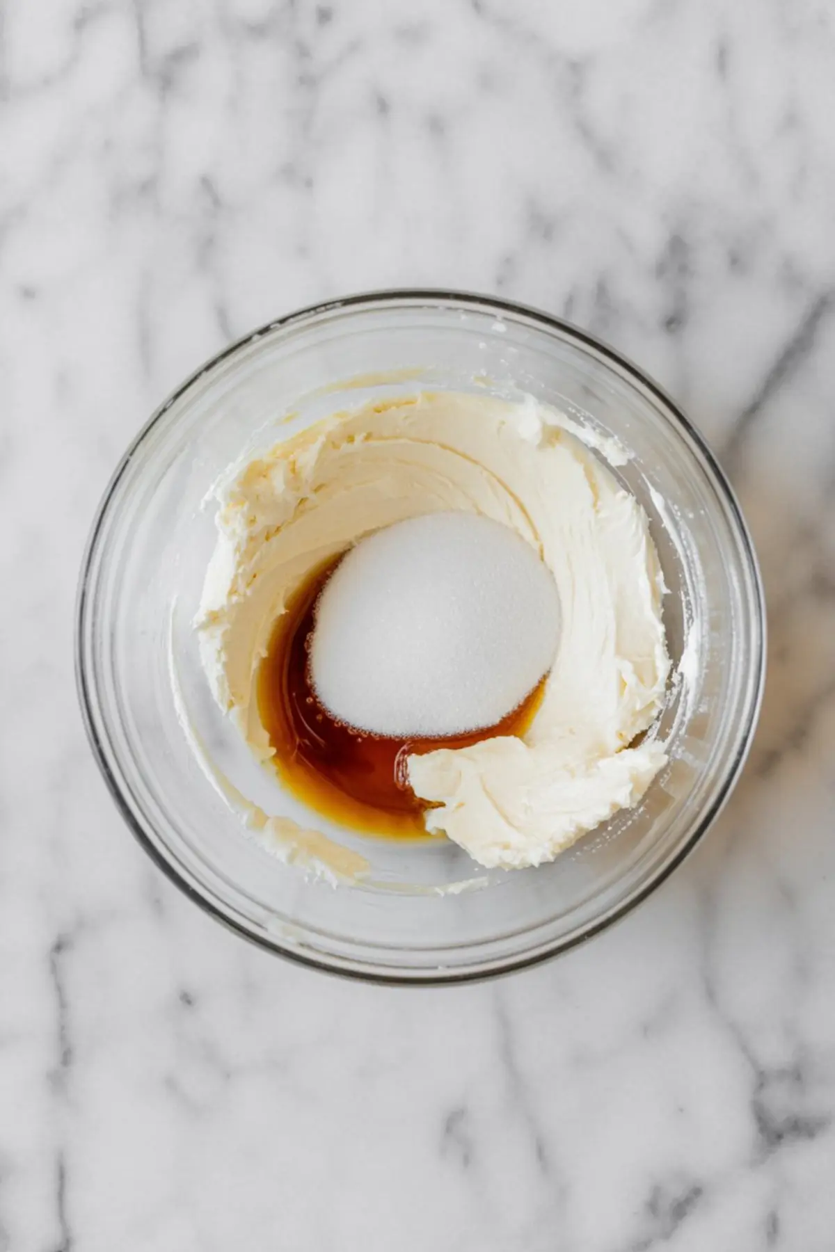 Cream cheese, sugar, and vanilla extract in a glass bowl ready to be blended for the creamy filling in pumpkin muffins.
