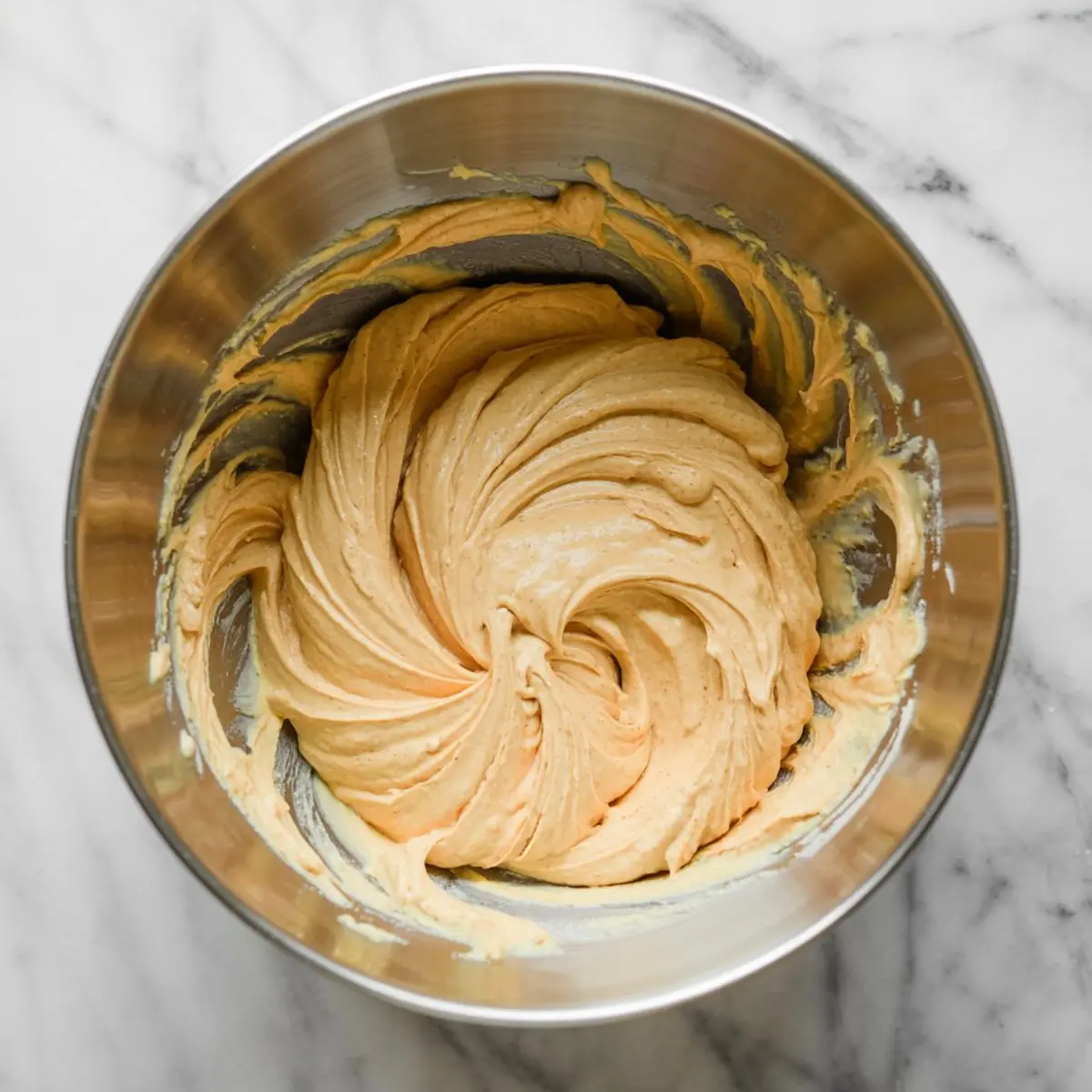 Smooth pumpkin cream cheese mixture swirled in a metal mixing bowl on a white marble countertop, ready for serving or spreading.