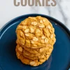 Close-up of a stack of soft and chewy pumpkin oatmeal cookies on a blue plate, topped with whole oats and set on a white marble surface with the text “Pumpkin Oatmeal Cookies” at the top.