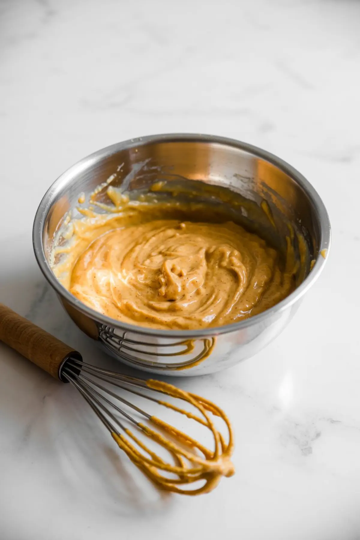 Stainless steel mixing bowl with thick pumpkin pie filling being whisked, showcasing creamy texture and rich orange color.