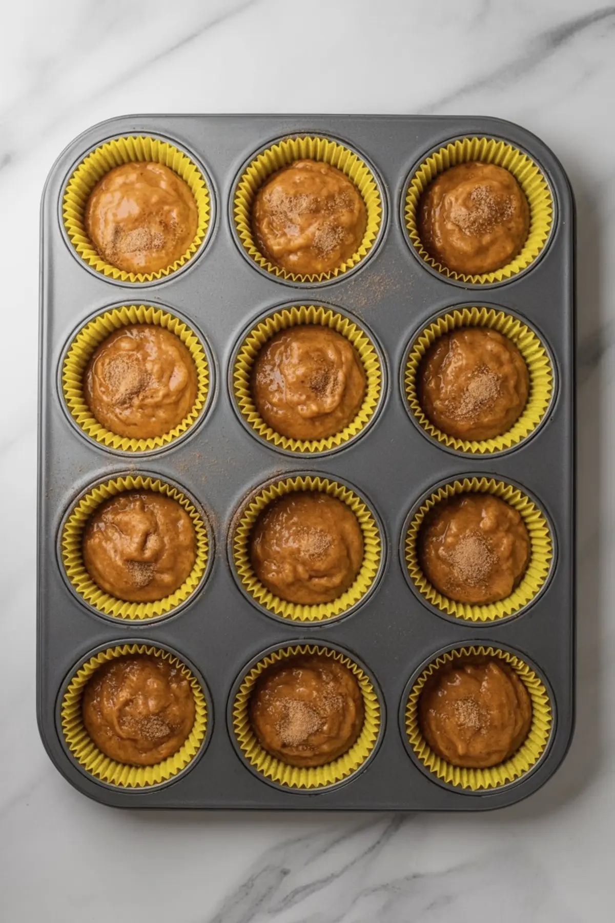 Yellow cupcake liners filled with pumpkin muffin batter in a muffin tin, ready to bake
