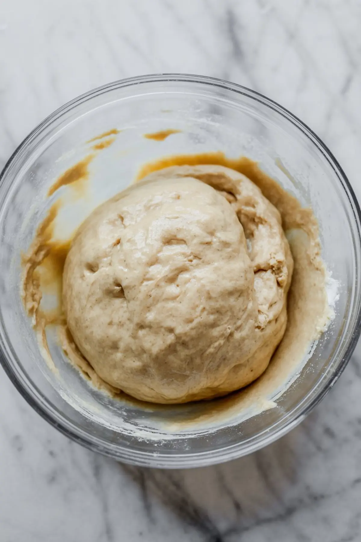 Sticky dough rising in a glass bowl with traces of flour and liquid on the sides.