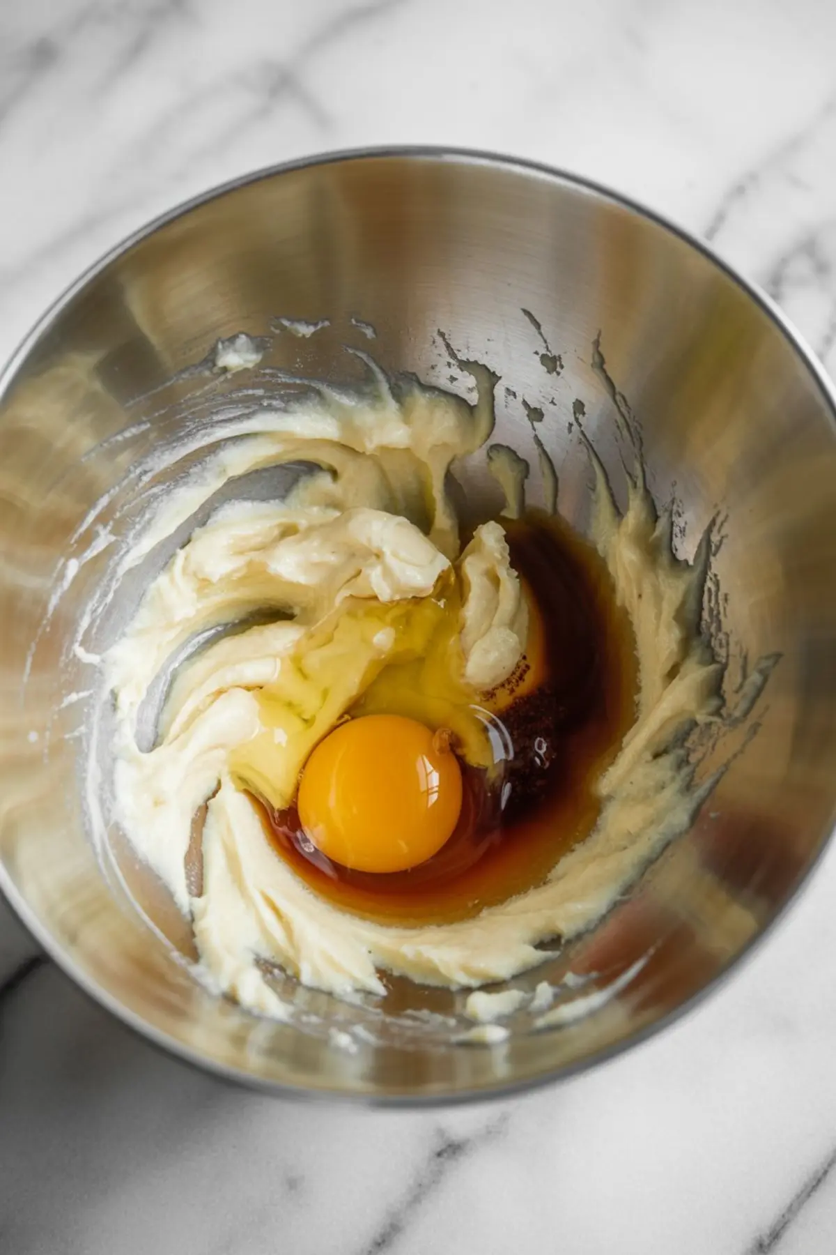 Stainless steel mixing bowl containing softened butter, a raw egg, and vanilla extract before mixing for a dessert recipe.