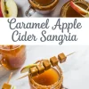 Caramel apple cider sangria served in mason jar mugs with cinnamon-sugar rims, garnished with apple slices and skewered caramel cubes, styled on a marble surface with text overlay in the center.