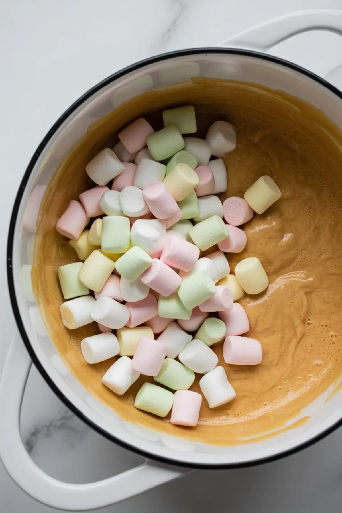 Pastel mini marshmallows added to a bowl of melted butterscotch and peanut butter mixture, captured mid-recipe preparation.