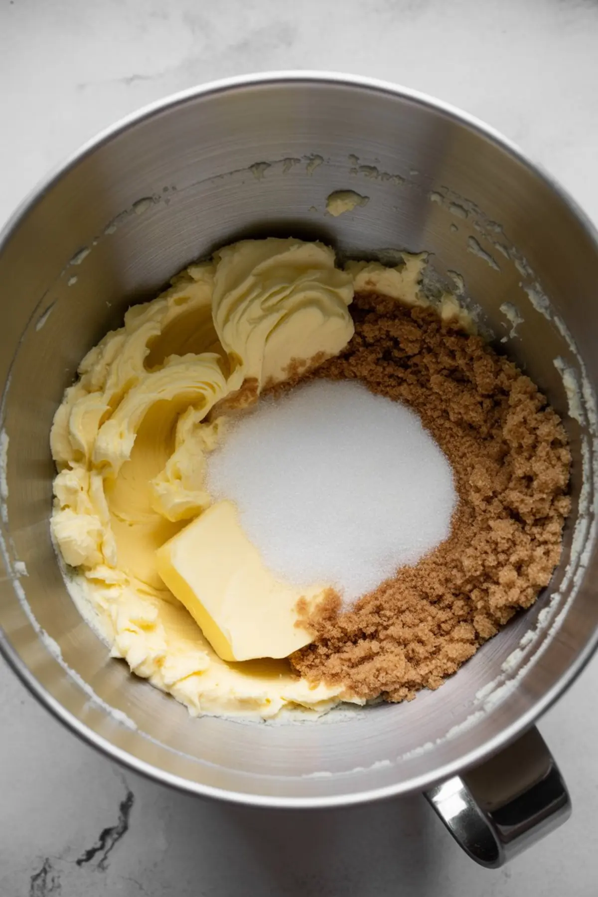 Mixing bowl with softened butter, brown sugar, and granulated sugar being creamed together as the base for cookie dough.