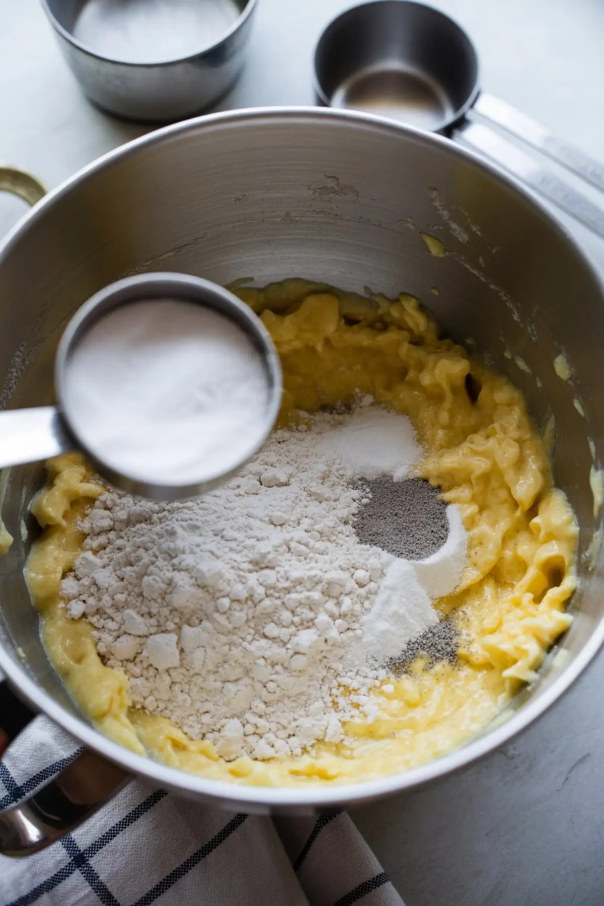 Mixing bowl with flour, sugar, and leavening agents added on top of a butter and egg mixture during cookie dough preparation.