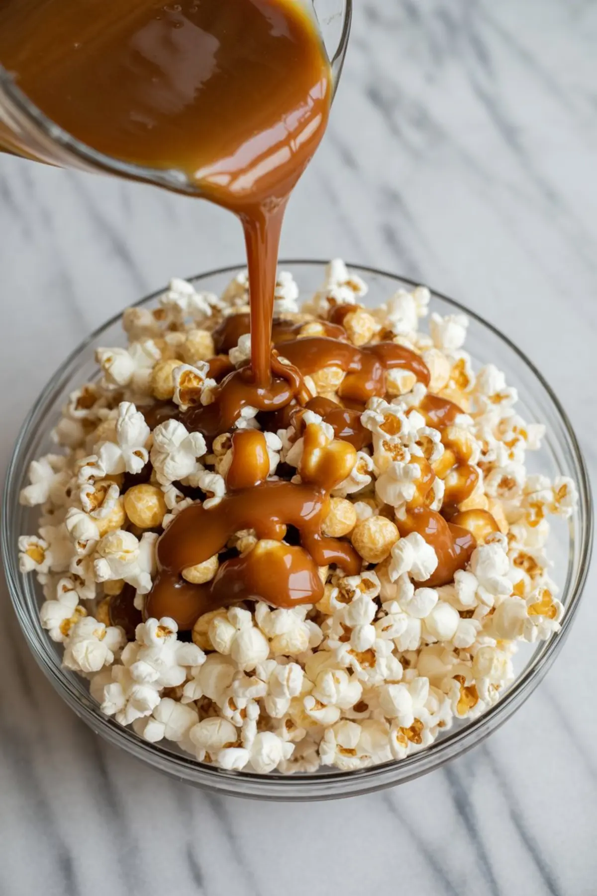 Close-up of rich caramel sauce being poured over a bowl of freshly popped popcorn, creating a sticky, golden coating for homemade caramel popcorn.