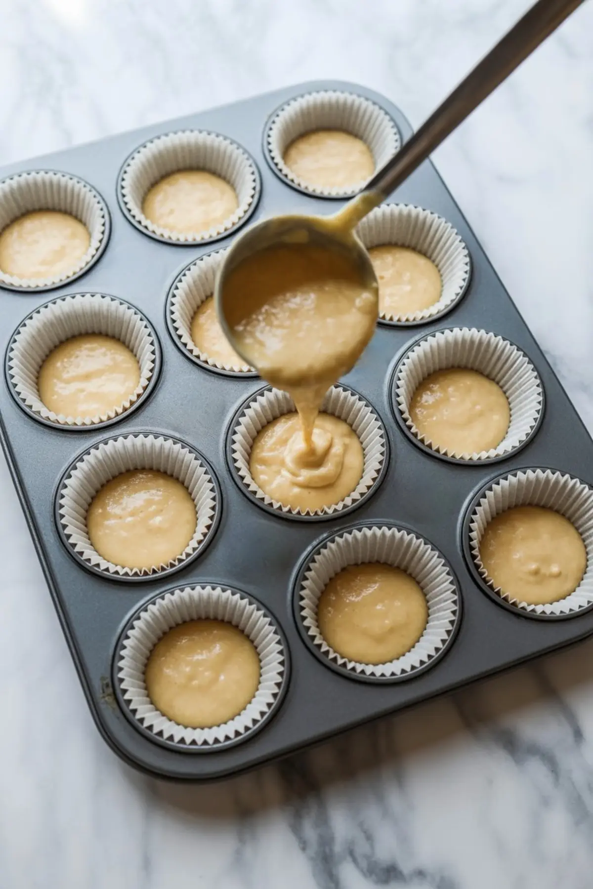Ladle pouring cheesecake batter into a muffin tin lined with paper cups, ready to be baked into cheesecake cups.