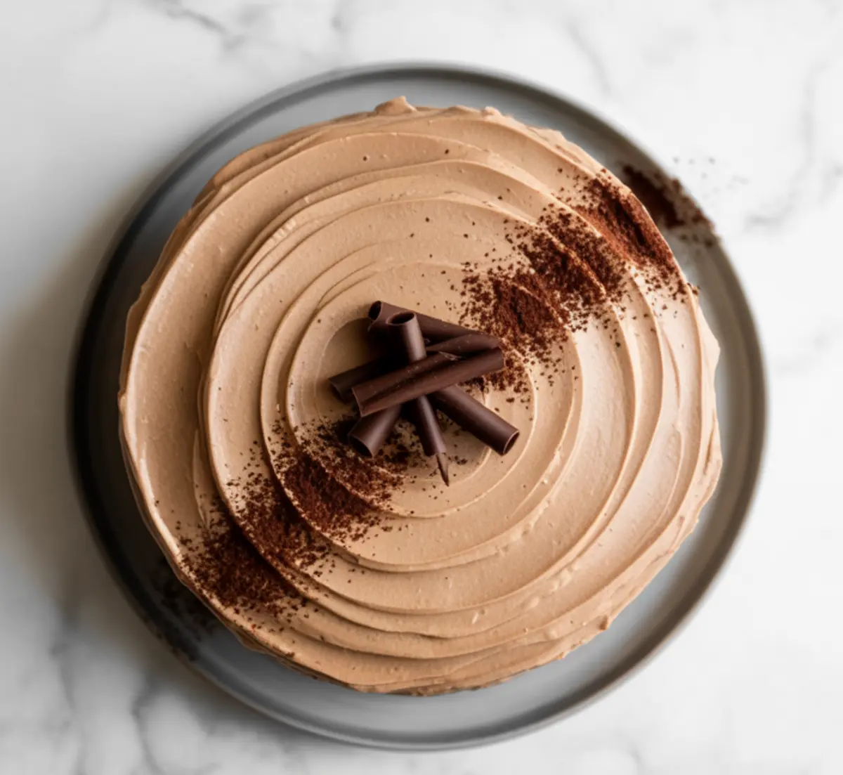 Top-down view of a chocolate espresso cake with silky coffee frosting, dusted cocoa powder, and decorative chocolate curls arranged at the center.