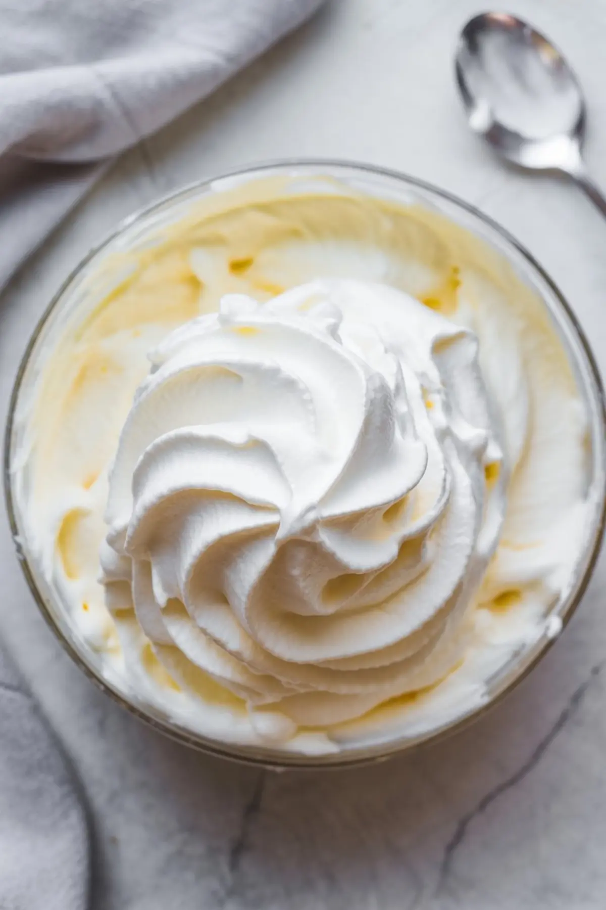 Close-up of creamy whipped topping in a glass bowl, swirled into soft peaks with smooth texture on a marble surface, perfect for dessert recipes and no-bake salads.
