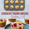 Golden cranberry orange muffins in a pan, with a halved muffin on a plate garnished with orange zest curls.