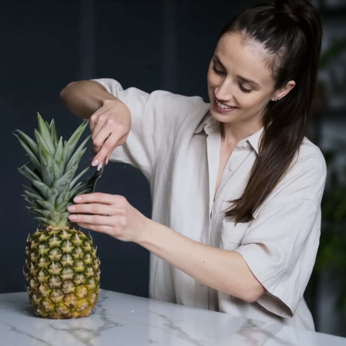 Emma slicing the top of a fresh pineapple on a marble countertop in a modern kitchen.