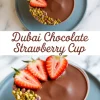 Top and angled view collage of a Dubai chocolate strawberry cup featuring a glossy chocolate surface topped with halved fresh strawberries and crushed pistachios, styled on a blue plate with elegant typography.