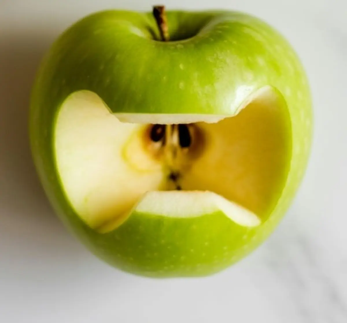 Green apple with a carved-out mouth shape revealing seeds and inner flesh, styled to resemble a monster face for Halloween snack ideas.