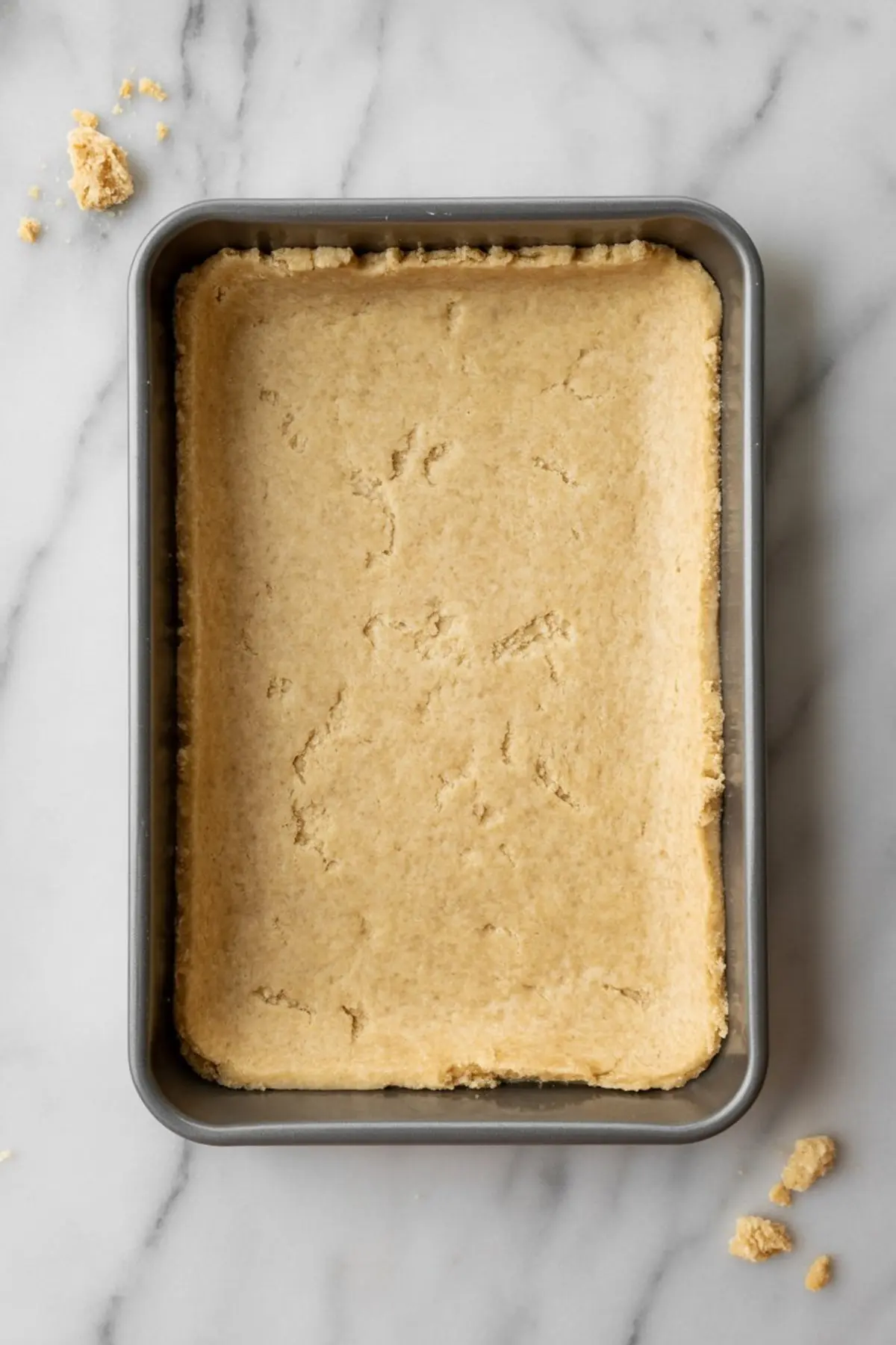 Rectangular baking pan filled with pressed shortbread crust dough, ready to be baked for lemon meringue pie bars.