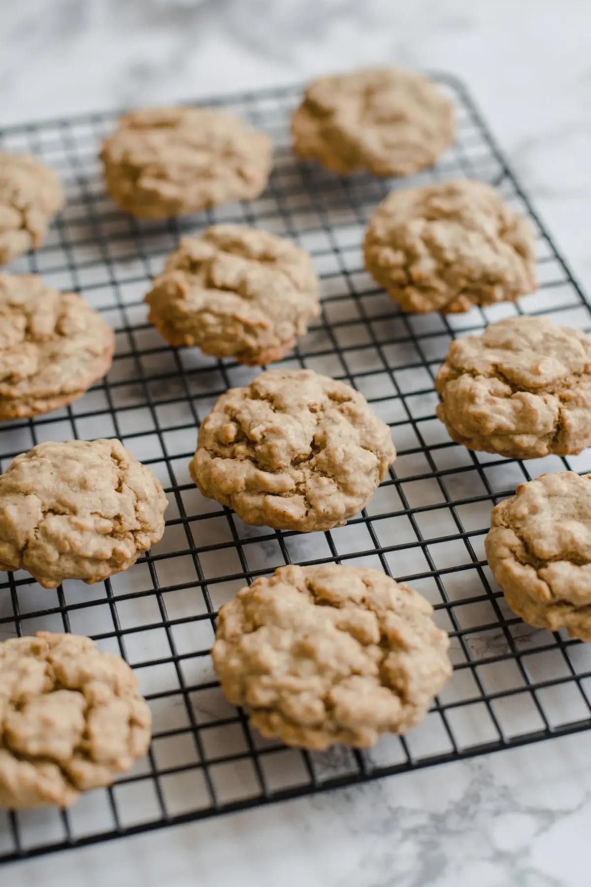 Freshly baked oatmeal cookies cooling on a wire rack, featuring a golden-brown surface and soft, chewy texture ideal for sandwiching cream filling.