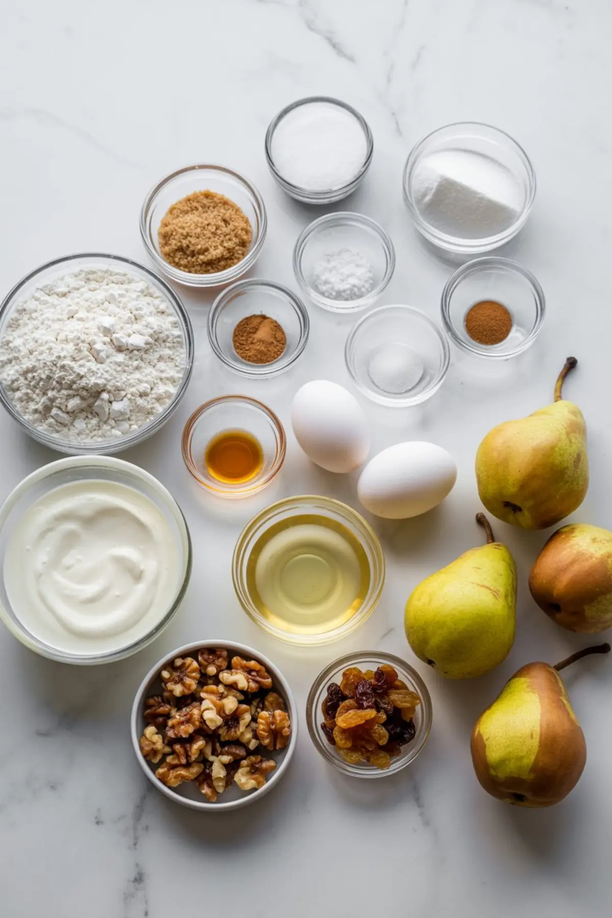 Flat lay of pear bread ingredients on a white marble surface, including flour, brown sugar, granulated sugar, cinnamon, baking powder, yogurt, eggs, vanilla extract, oil, walnuts, golden raisins, and whole pears.
