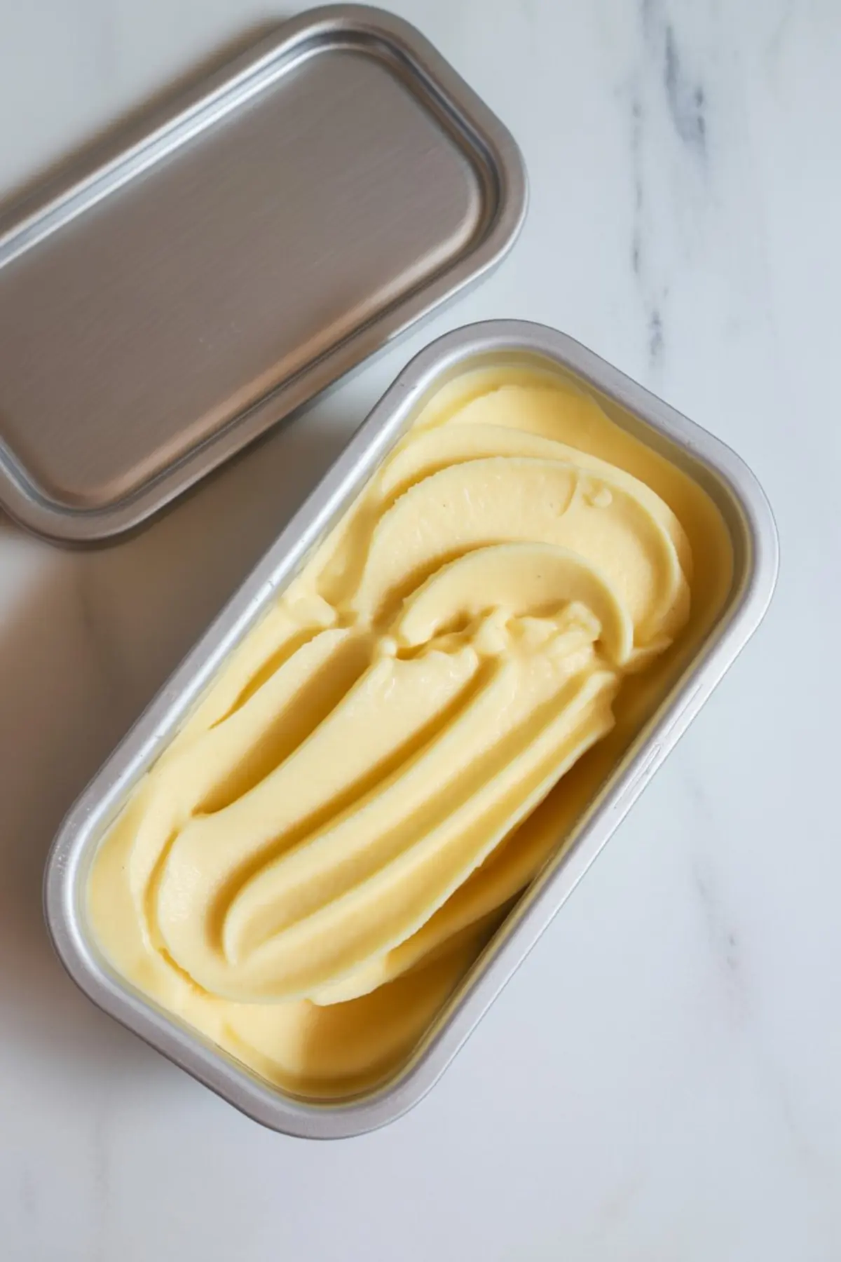 Freshly made creamy pineapple sorbet in a metal container on a white marble surface.