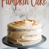Homemade pumpkin cake with cream cheese frosting on a cake stand, topped with a light dusting of cinnamon, with text overlay reading “Pumpkin Cake with Cream Cheese Frosting.”