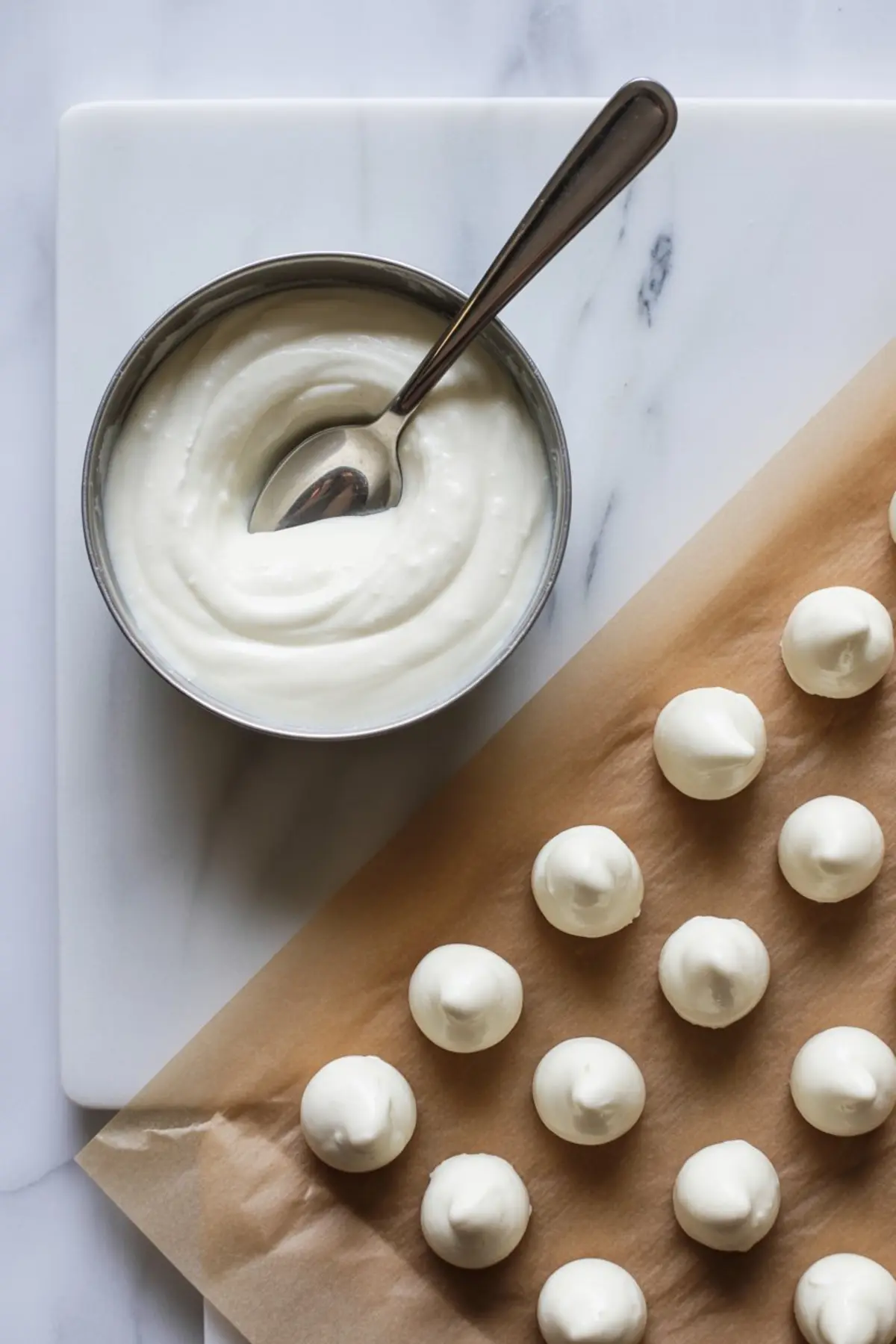 Thick pumpkin cookie dough with a rich orange hue in a stainless steel mixing bowl, stirred with a grey silicone spatula on a white marble countertop.