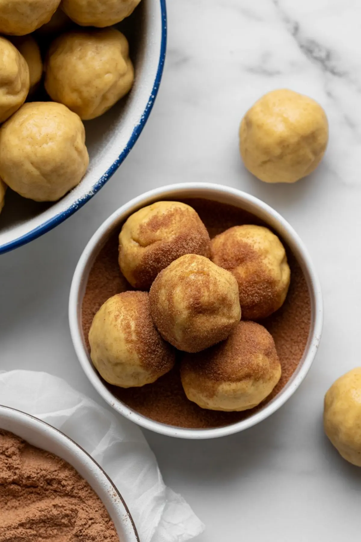 Overhead view of dry baking ingredients including flour, cinnamon, ginger, sugar, baking powder, and ground spices arranged in a mixing bowl on a white marble surface.