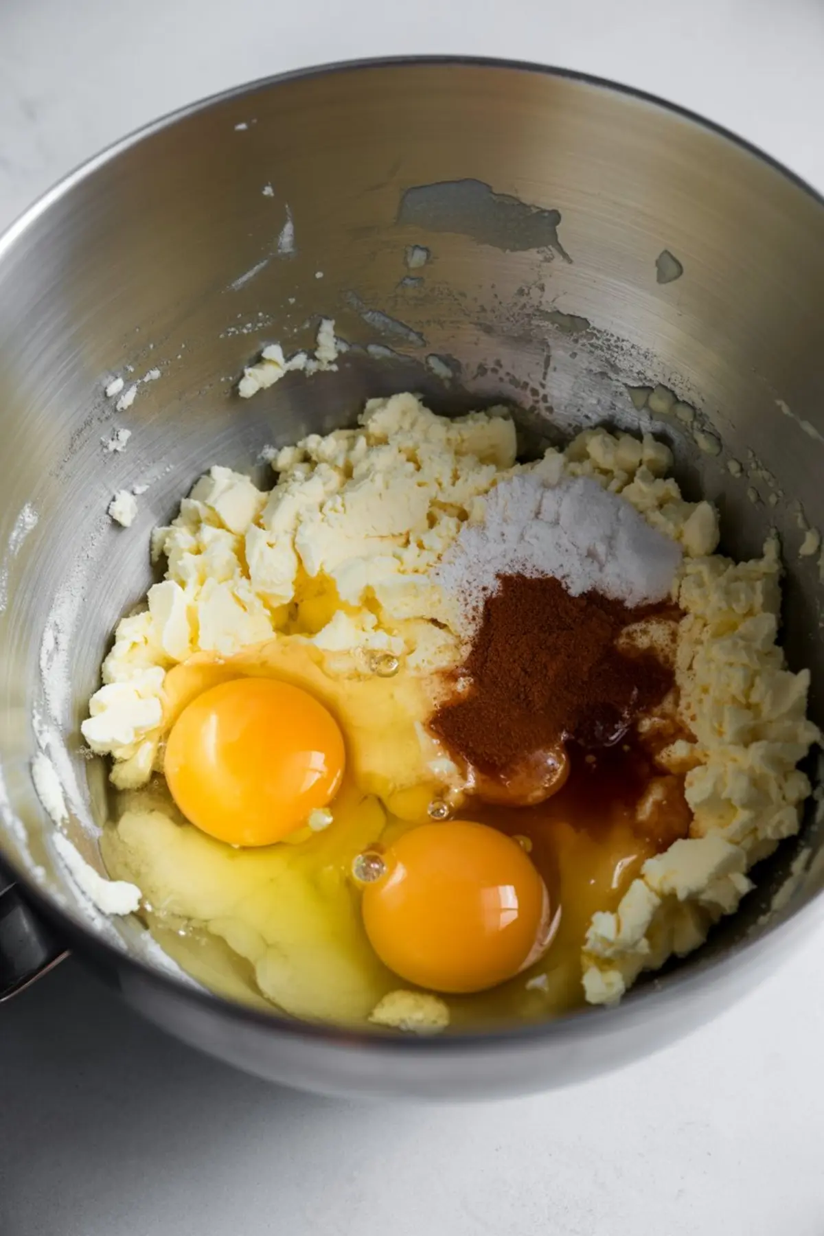Mixing bowl filled with cookie dough ingredients including softened butter, eggs, cinnamon, sugar, and vanilla extract for baking salted caramel cookies.
