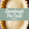 Unbaked sourdough pie crust in a glass pie dish with crimped edges, set on a pink plate, with text overlay reading “Sourdough Pie Crust Recipe.”