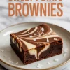 Single sweet potato brownie with a striking cream cheese swirl and flaky salt flakes, served on a white plate with text overlay reading “Sweet Potato Brownies” in bold orange letters.