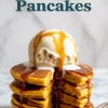 Tall stack of sweet potato pancakes split down the middle, topped with melting vanilla ice cream and rich caramel drizzle, with bold text reading “Sweet Potato Pancakes.”