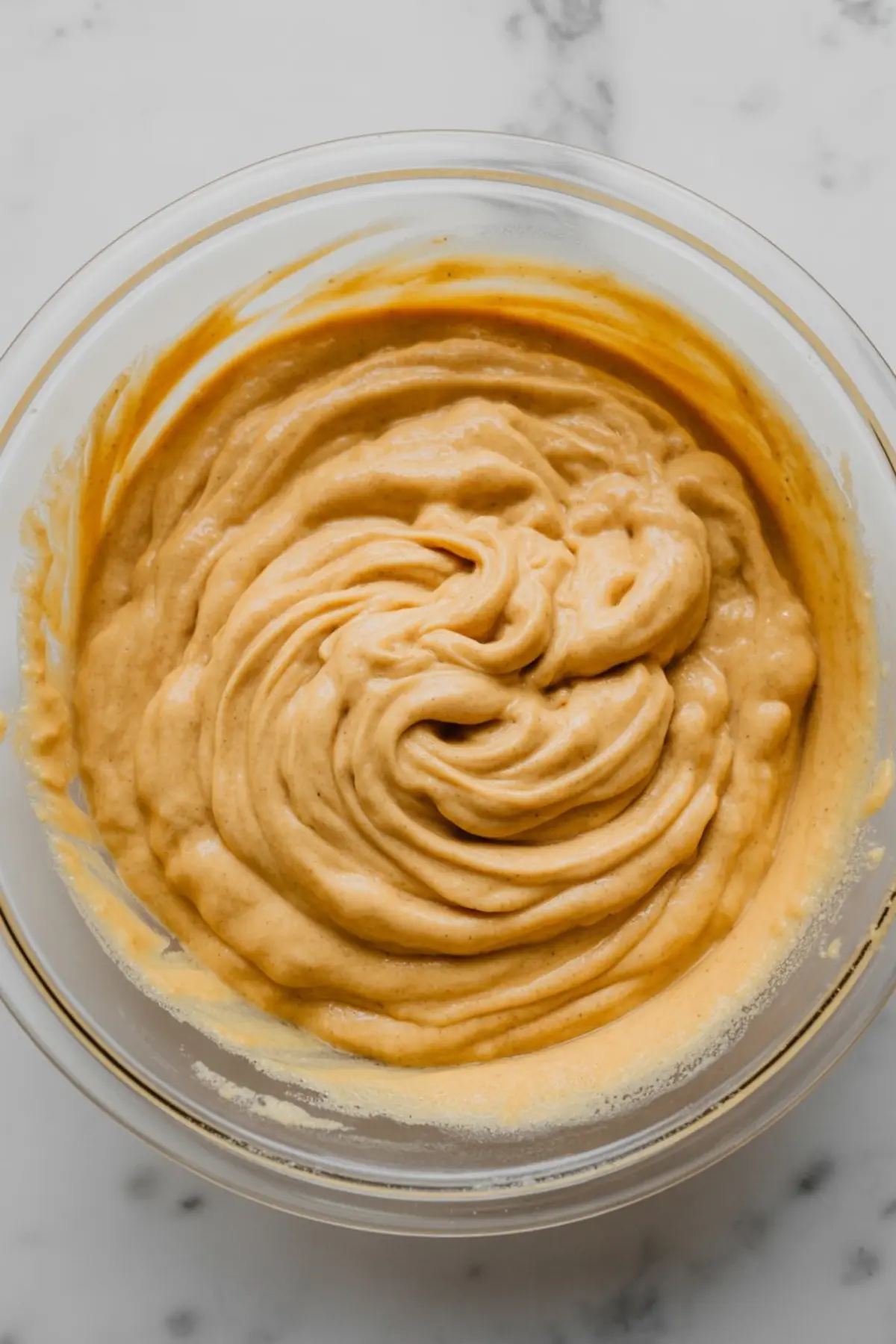 Creamy blended sweet potato pancake batter in a clear glass bowl, swirled and ready for cooking.