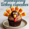 Single chocolate turkey cupcake topped with swirled chocolate frosting and candy corn feathers, placed on a white ceramic plate with a marble background and “thanksgiving turkey cupcakes” text overlay.