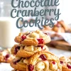Stack of golden white chocolate cranberry cookies on parchment paper, with chunks of white chocolate and dried cranberries visible, styled under a handwritten text overlay that reads “White Chocolate Cranberry Cookies.”