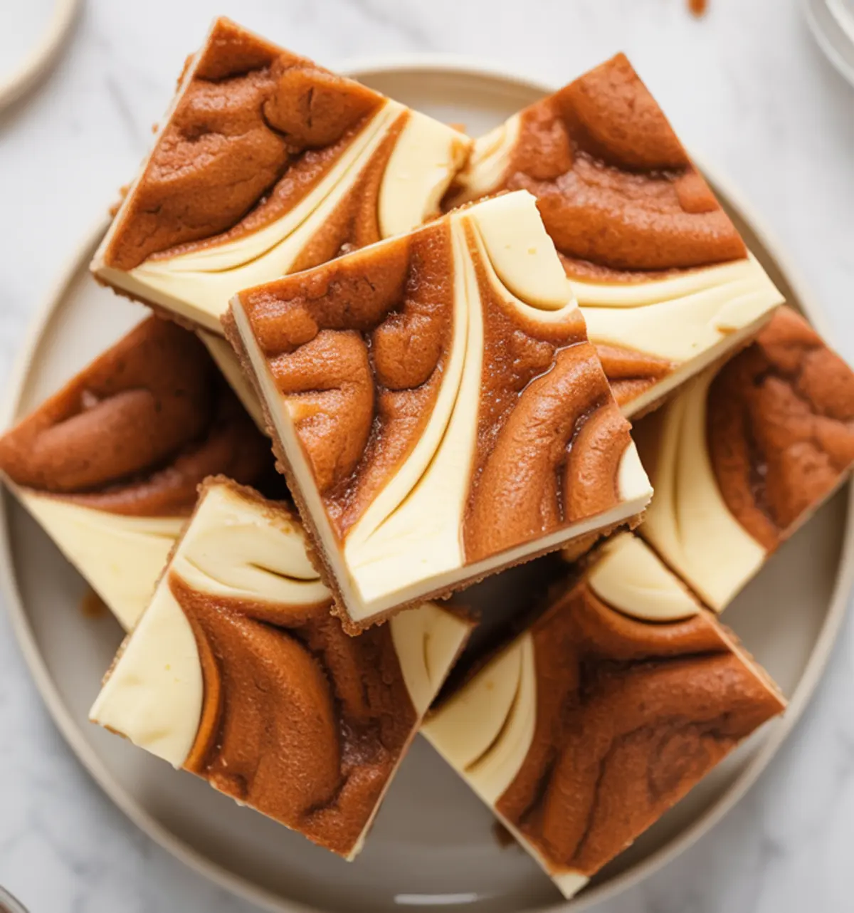 Plate of cheesecake swirl snickerdoodle bars arranged in a circular pattern, showcasing defined cinnamon cookie swirls on creamy cheesecake squares.