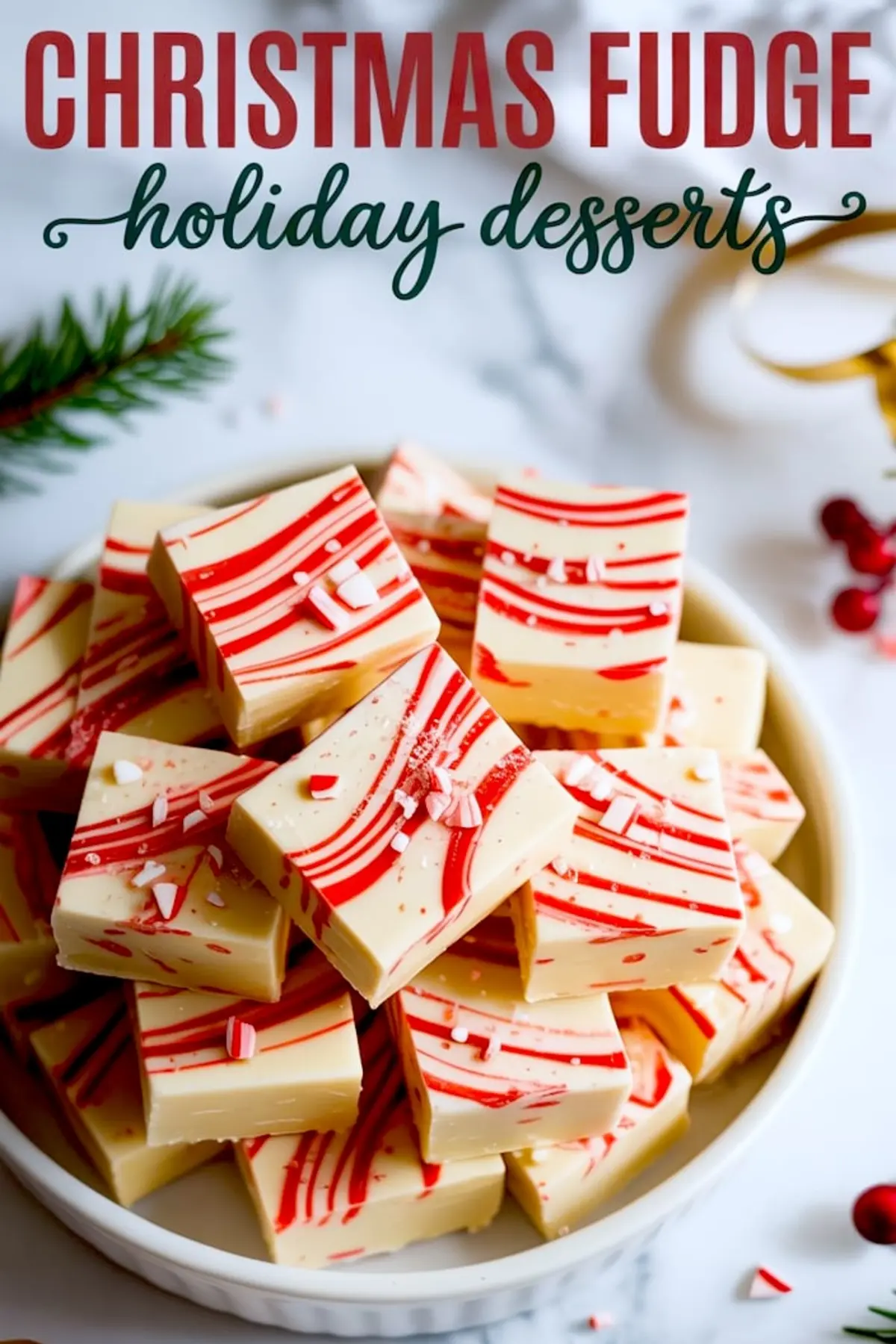 Close-up of white chocolate peppermint fudge with red swirl pattern and crushed candy cane pieces stacked in a white bowl, styled on a marble surface with pine and ribbon for holiday dessert inspiration.