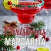 Christmas margarita cocktail in a wide glass with green sugar rim, garnished with a lime wheel and fresh cranberry, surrounded by pine branches and cranberries.