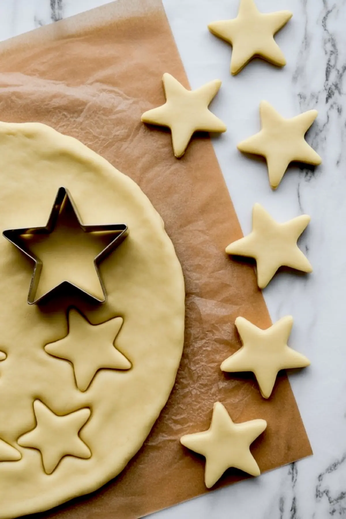 Star-shaped cookie cutter pressed into rolled-out pie dough on parchment paper with cut-out stars arranged nearby for decorative pie topping.
