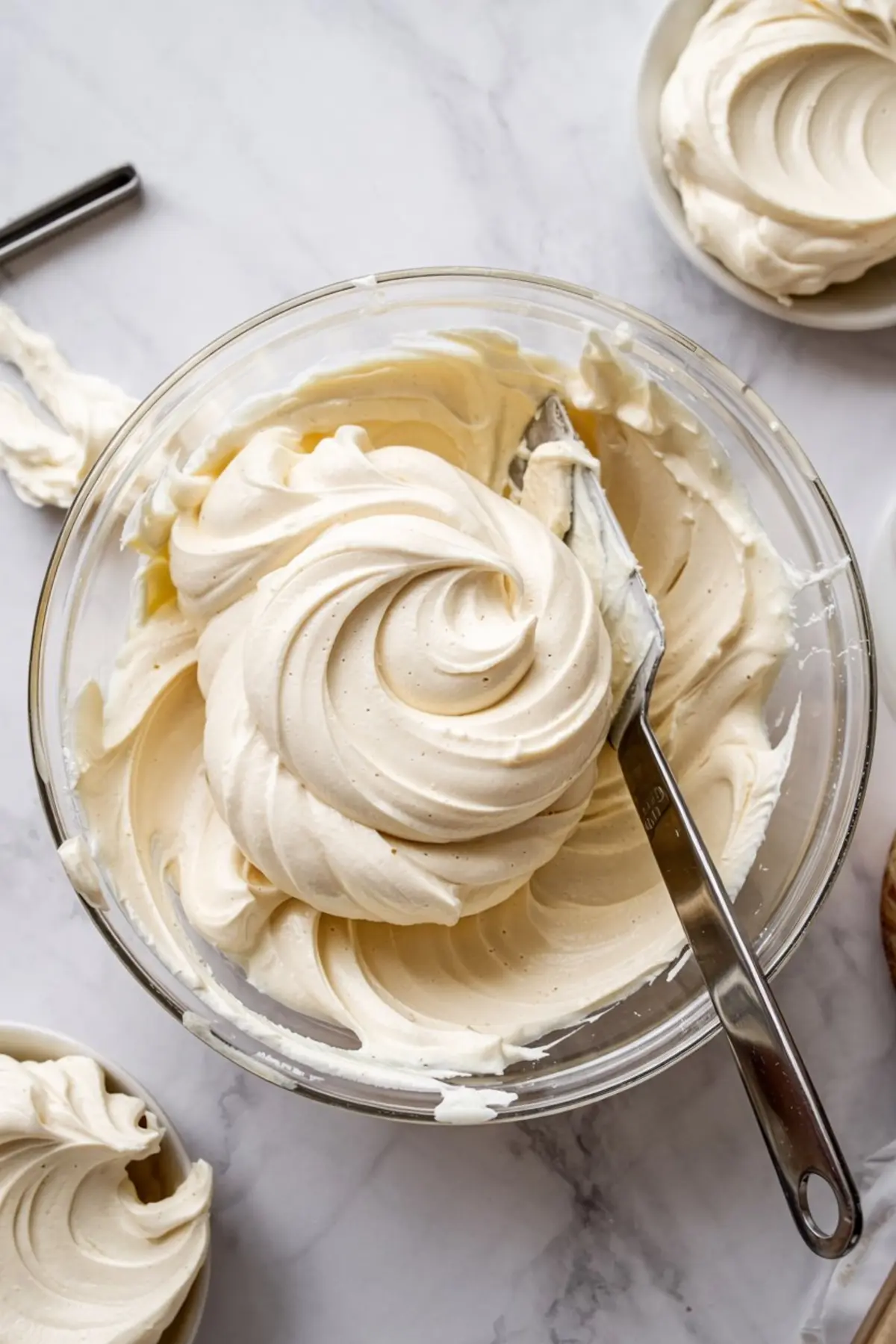 Fluffy vanilla buttercream frosting swirled in a glass bowl with a metal spatula, perfect for spreading on sugar cookie bars.