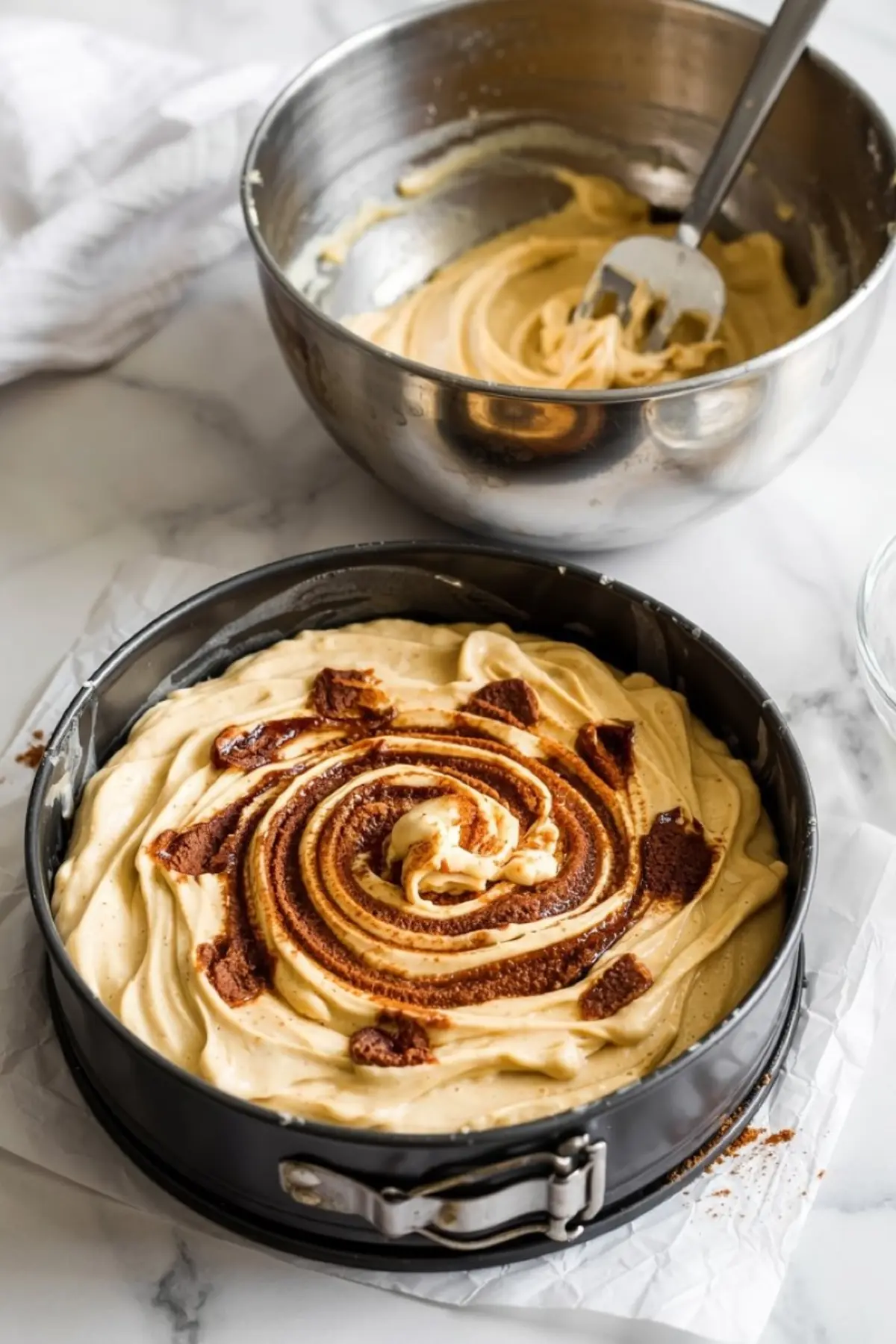 Unbaked cinnamon coffee cake batter in a round springform pan, topped with a visible swirl of cinnamon-sugar mixture, sitting next to a mixing bowl.