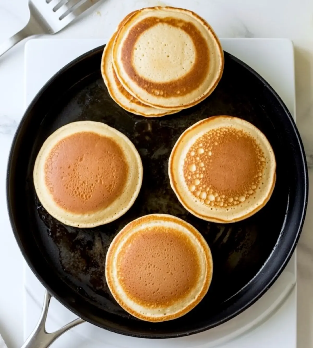 Golden brown cinnamon pancakes cooking on a nonstick skillet, showing evenly browned tops and bubbly textures during the frying process.